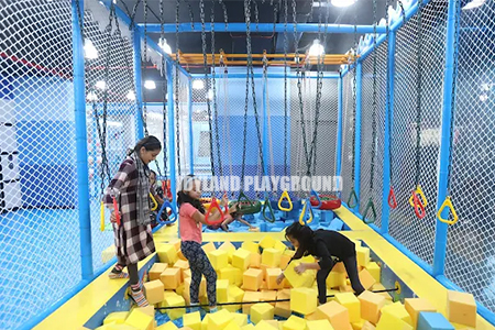 Kids navigating a ninja warrior obstacle course in an indoor playground in India.