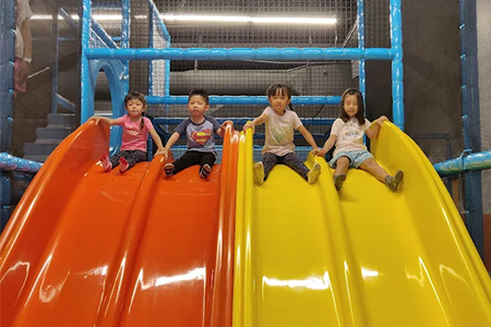Children racing down a four-lane slide in an indoor playground.