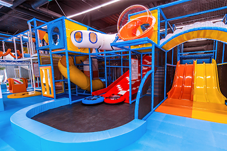 Children playing in a soft play area with colorful foam shapes in an indoor playground.
